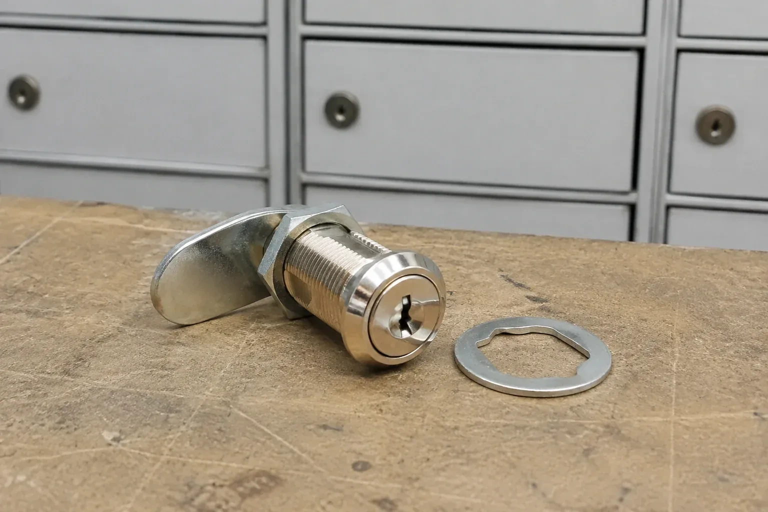 Detached threaded cam lock and mounting washer on a workbench in front of closed mail compartments. — Mailbox Lock Replacement, London